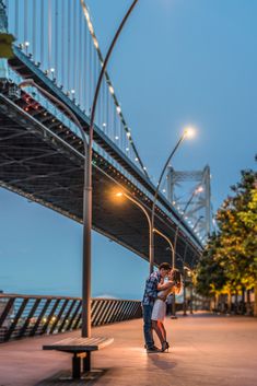 a man and woman standing under a bridge at night with their arms around each other