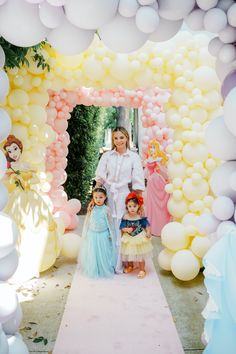 a woman and two children standing in front of a balloon arch with princesses on it