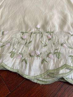 a white sheet with pink flowers and green leaves on it sitting on a wooden floor