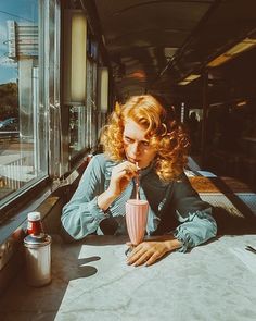 a woman sitting at a table with a drink in her hand and looking out the window