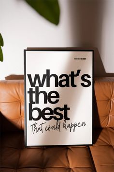 a black and white sign sitting on top of a brown leather couch next to a potted plant