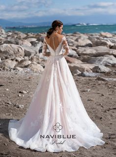 a woman in a wedding dress standing on rocks near the ocean with her back to the camera