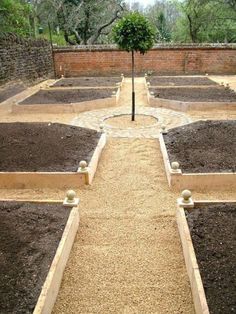 a garden with many different types of plants and dirt on the ground in front of a brick wall