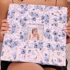 a woman holding up a blue and white photo frame with a flower pattern on it