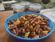 a blue bowl filled with nuts sitting on top of a wooden table next to jars