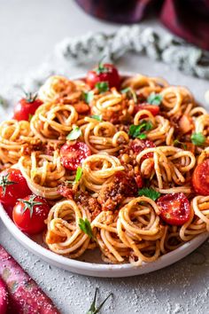 a plate full of spaghetti with tomatoes and meat on the side, next to some parsley