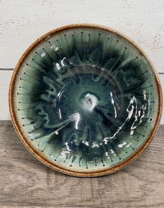 a green and brown bowl sitting on top of a wooden table next to a white wall