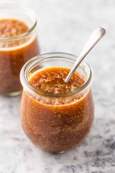 two jars filled with sauce sitting on top of a marble counter next to each other