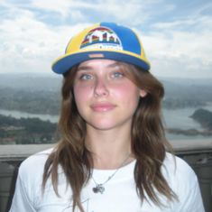 a young woman wearing a hat and looking at the camera while standing on top of a building