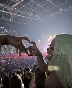 a woman with long blonde hair making a heart sign in front of an audience at a concert