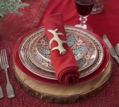 a place setting with red napkins and silverware on a wood slice table cloth