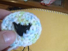 a hand holding a small crocheted object with a black bird on it