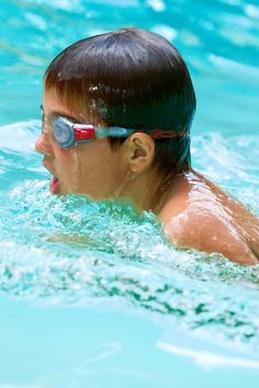 a young boy swimming in a pool with goggles on