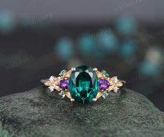 a green ring with three different colored stones on it's side, sitting on top of a rock