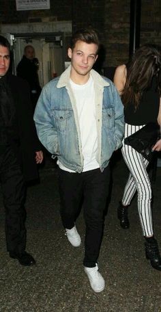 a young man and woman are walking down the street at night, one is wearing a jean jacket