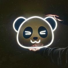 a person holding up a lit up panda bear mask in front of their face with eyes closed