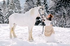 a woman standing next to a white horse in the snow