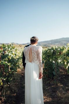 the back of a bride's dress as she stands in front of a vineyard