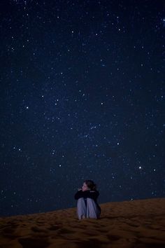 a person sitting in the sand looking up at the stars