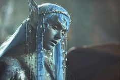 a woman with blue hair and beads on her head is staring at something in the distance