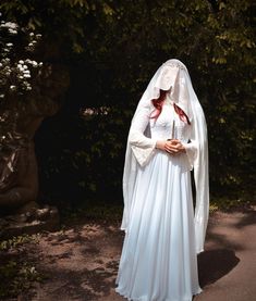 a woman in a white wedding dress and veil standing on a path with trees behind her