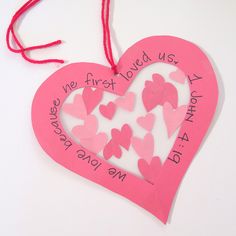 a pink heart shaped ornament hanging from a red string on a white surface