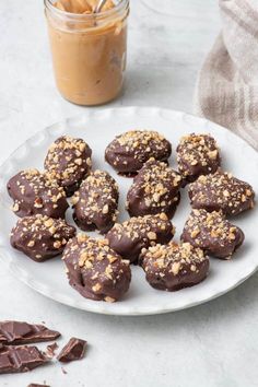 chocolate covered cookies on a white plate next to a jar of peanut butter and cinnamon sticks