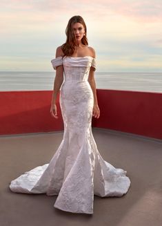 a woman in a white dress is standing on a balcony near the ocean and looking at the camera