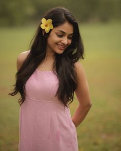 a woman in a pink dress with a yellow flower in her hair smiles at the camera