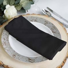 a place setting with black napkins and silverware on a wood sliced table