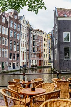 tables and chairs are lined up along the water in front of some buildings with windows