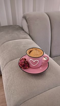 a cup of hot chocolate on a pink saucer next to a flower in front of a gray couch