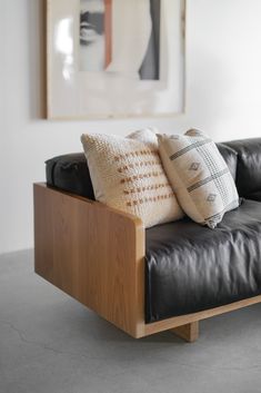 a black leather couch with two pillows on it and a painting in the back ground