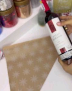 a person holding a bottle of wine in front of a counter with other bottles on it