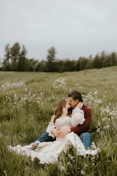 a man and woman are sitting in the grass with their arms around each other as they kiss