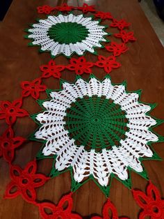 three crocheted doily on a wooden table with red, white and green flowers