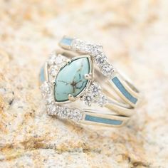 a turquoise stone and diamond ring sitting on top of a rocky surface with white stones