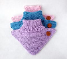 three knitted bibs with brown buttons are shown on a white surface, one is pink and the other is blue