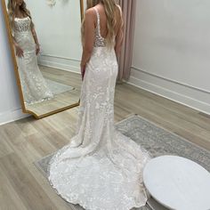 a woman standing in front of a mirror looking at her wedding dress on the floor