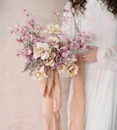 two women in white dresses holding bouquets of pink and beige flowers with ribbons tied around them