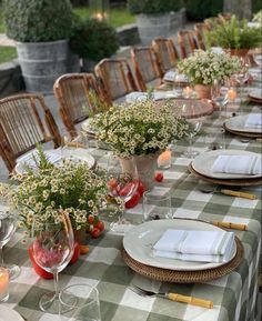 an outdoor table set with place settings and flowers in vases on the tablescloth