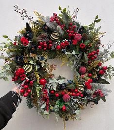 a wreath with red berries and greenery is being held by someone's hand