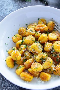 a white bowl filled with potatoes covered in parmesan cheese and garnished with herbs