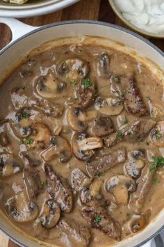 a large pot filled with mushrooms and sauce on top of a wooden table next to bread