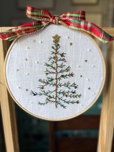 a cross - stitch christmas tree is hanging on a wooden easel with a red ribbon