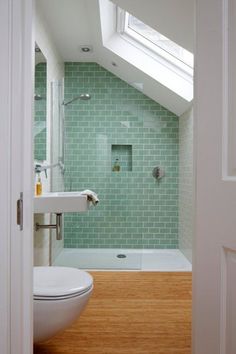 an open door leading to a bathroom with green tiles on the walls and wood flooring