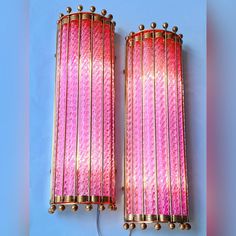 two pink and gold wall lights on a blue background, one is plugged in