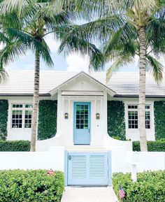 a white house with blue shutters and two palm trees in front of the door