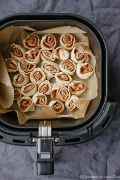 some food is sitting in a black container on a gray table cloth and it looks like they have rolled up cinnamon rolls