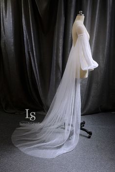 a white veil on top of a mannequin's head in front of a black curtain